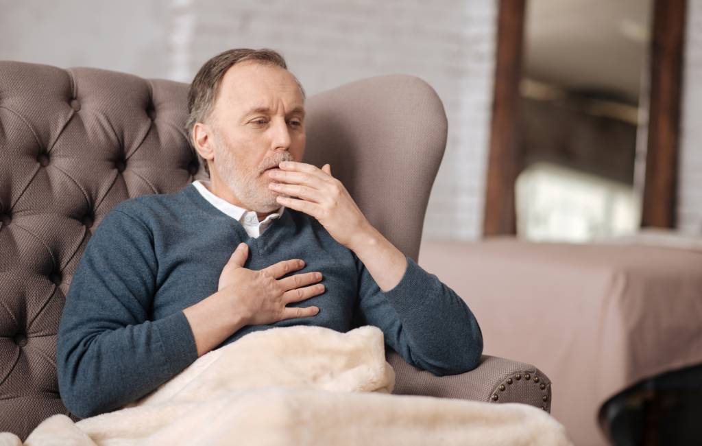 Old man sitting on couch and coughing