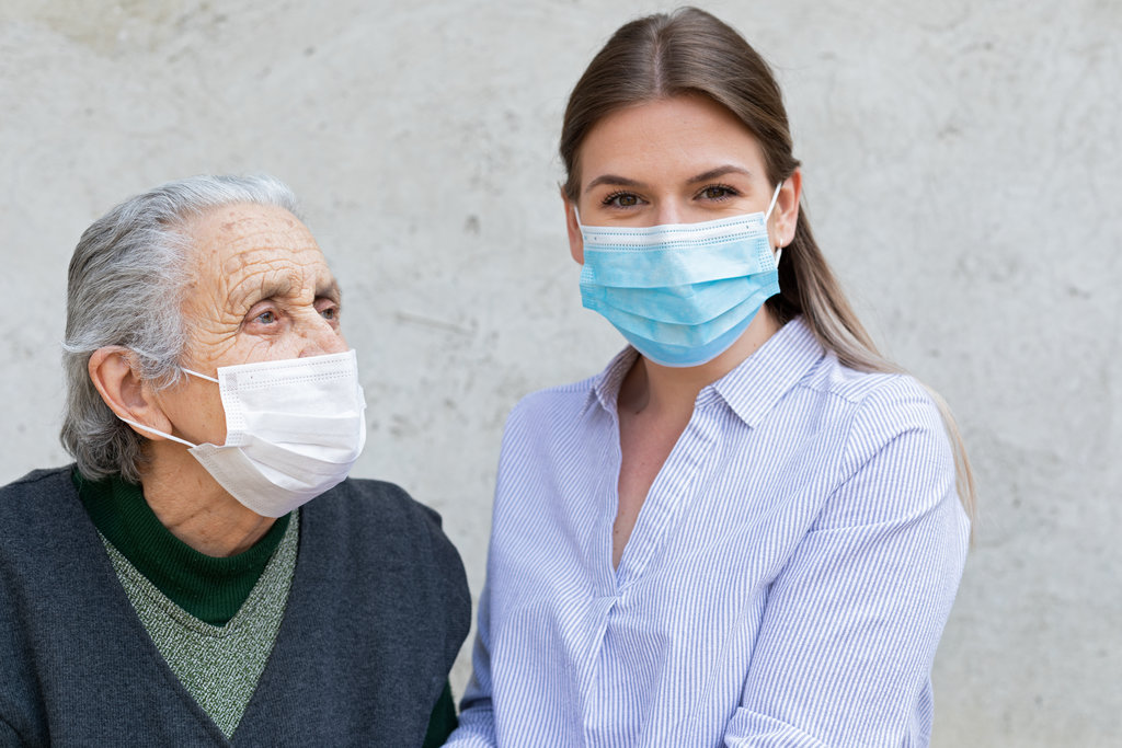 Caregiver with elderly ill woman wearing mask