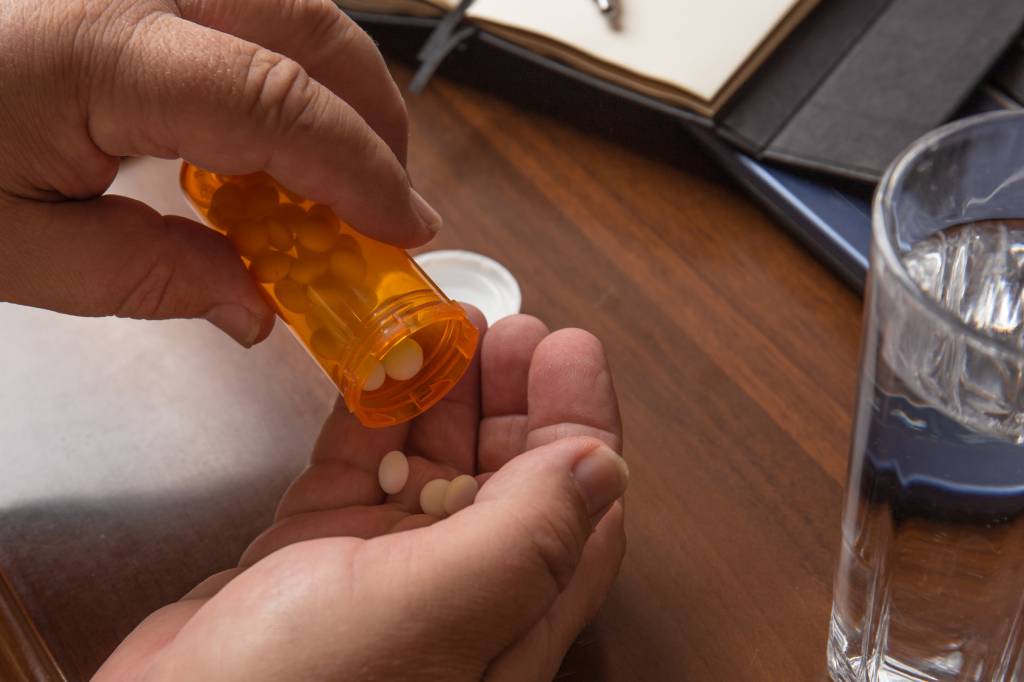 Elderly man with pill or drug tablet or medication in hand and glass of water at home