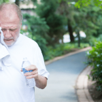 Senior wiping sweat and drinking water from the heat