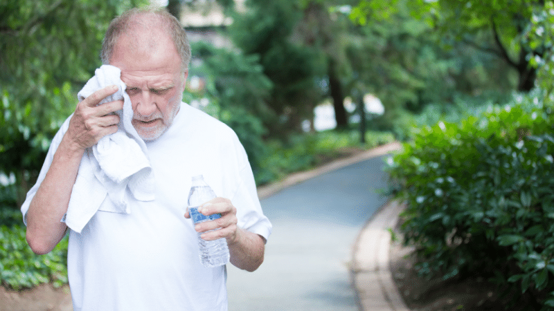 Senior wiping sweat and drinking water from the heat